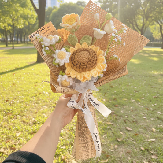 Hand holding a bouquet of knitted flowers with a sunflower design against a park background