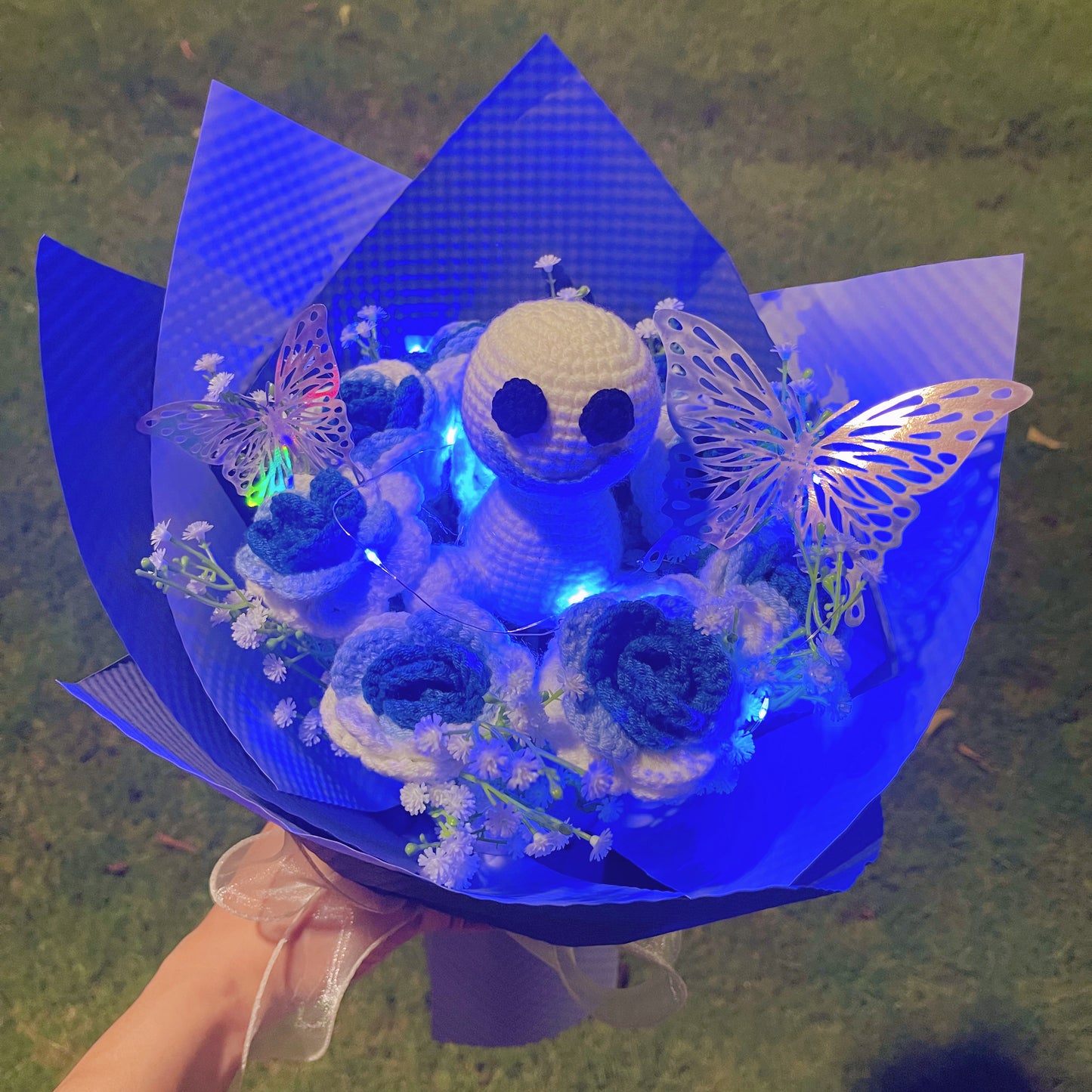 Gefrorener Rosenstrauß mit Farbverlauf von Weiß nach Blau, weißem Schleierkraut und leuchtend bunten Schmetterlingsakzenten, wunderschön verpackt in hell- und dunkelblauem Papier, ideal für Feiern im Prinzessinnenstil.