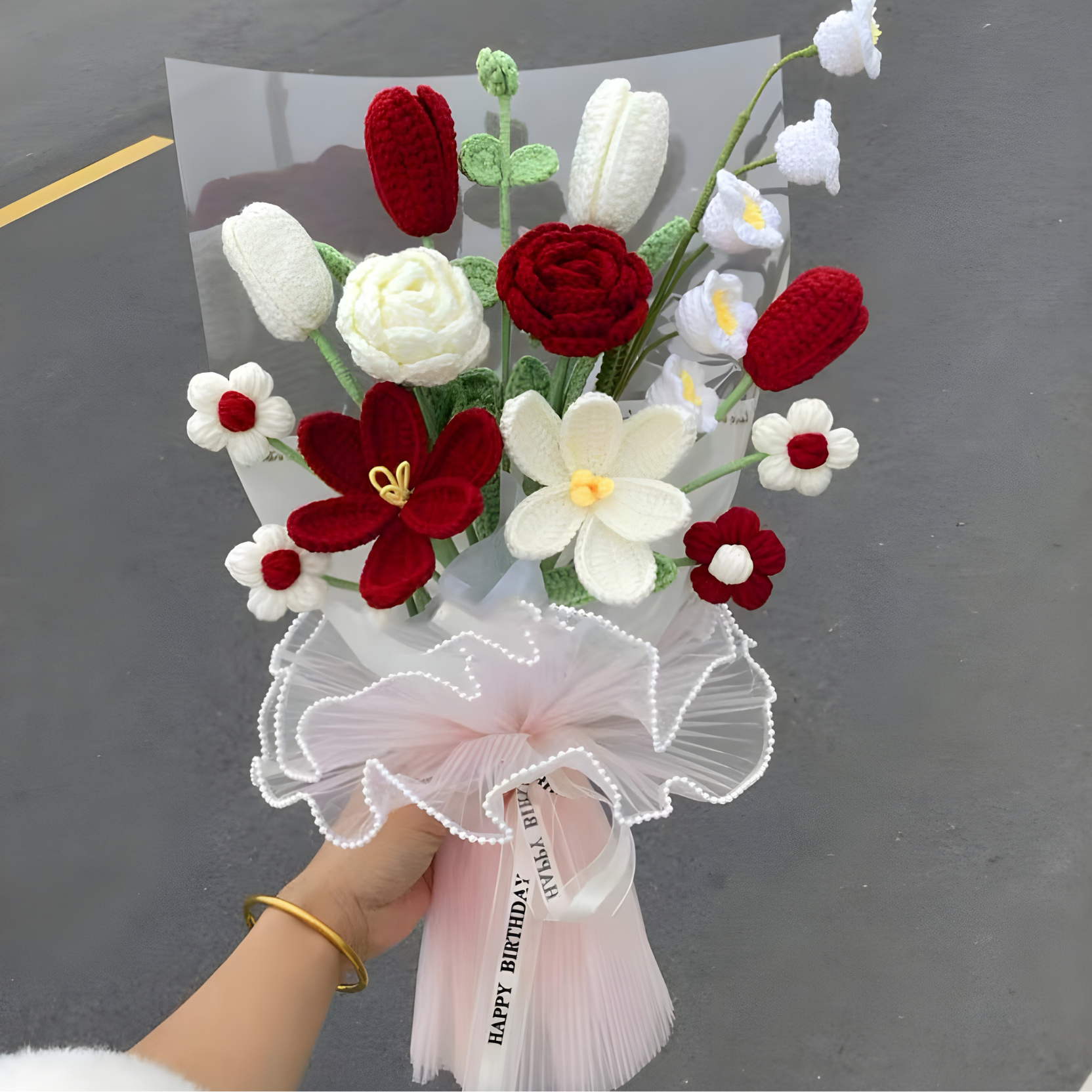 Bouquet of red, white, and green flowers held by a person against a dark background