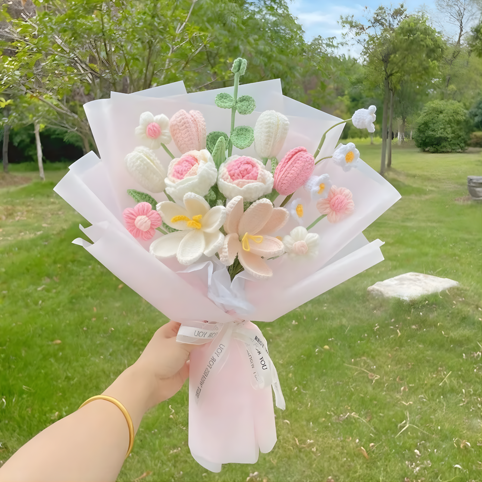 Bouquet of pink and white flowers held by a person outdoors with greenery in the background