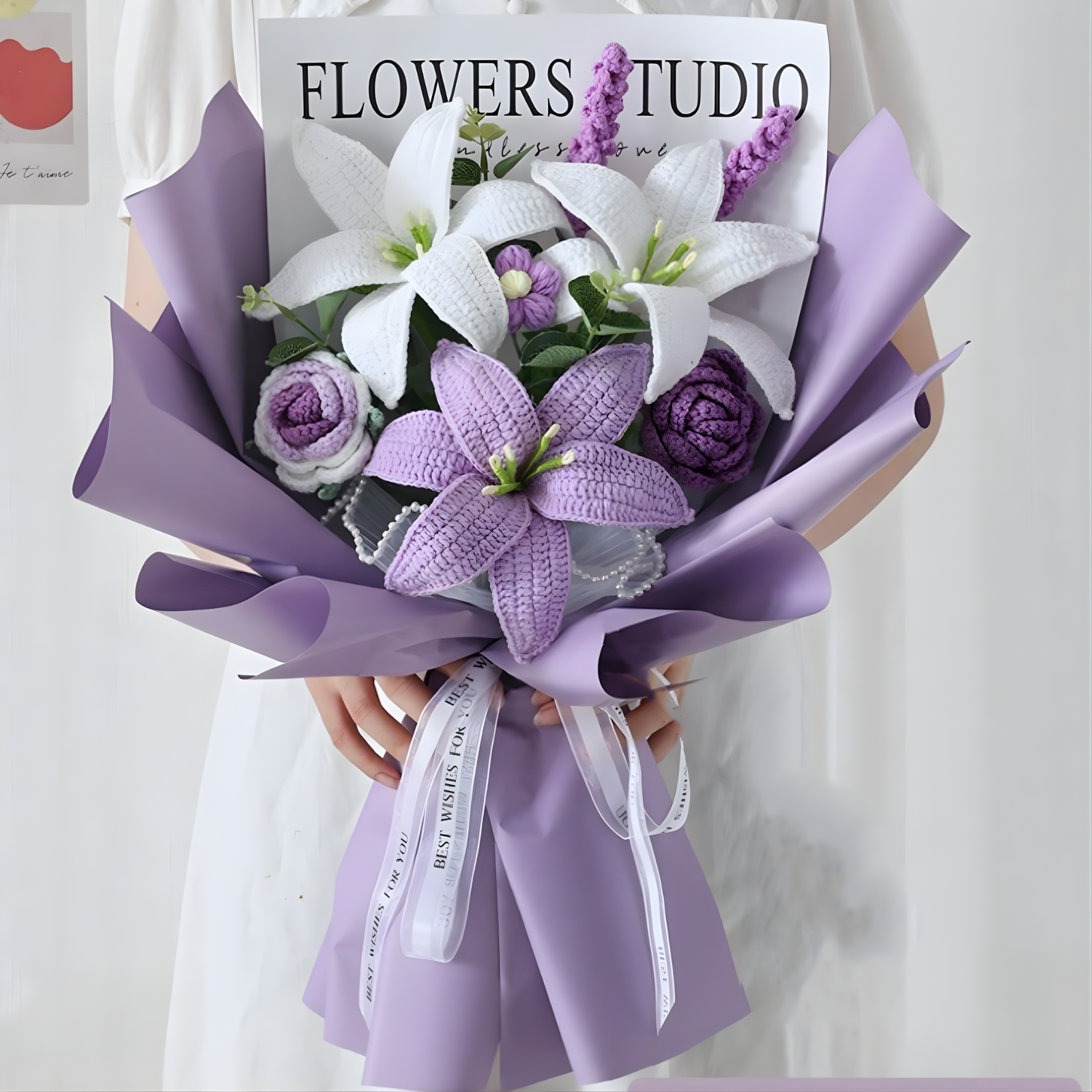 Bouquet of white and purple flowers in a purple wrap held by a person with 'Flowers Studio' sign in the background.