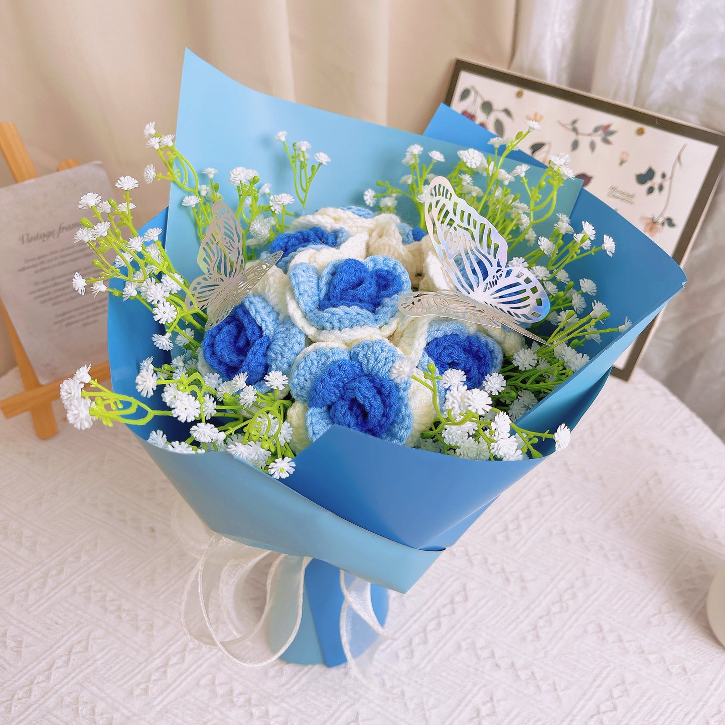 Bouquet de Roses Gradientes de Branco a Azul Congeladas com Espinhas de Bebê Branco e Acentos Vibrantes de Borboletas Coloridas, Belamente Embalado em Papéis Azul Claro e Escuro, Ideal para Celebrações como de uma Princesa