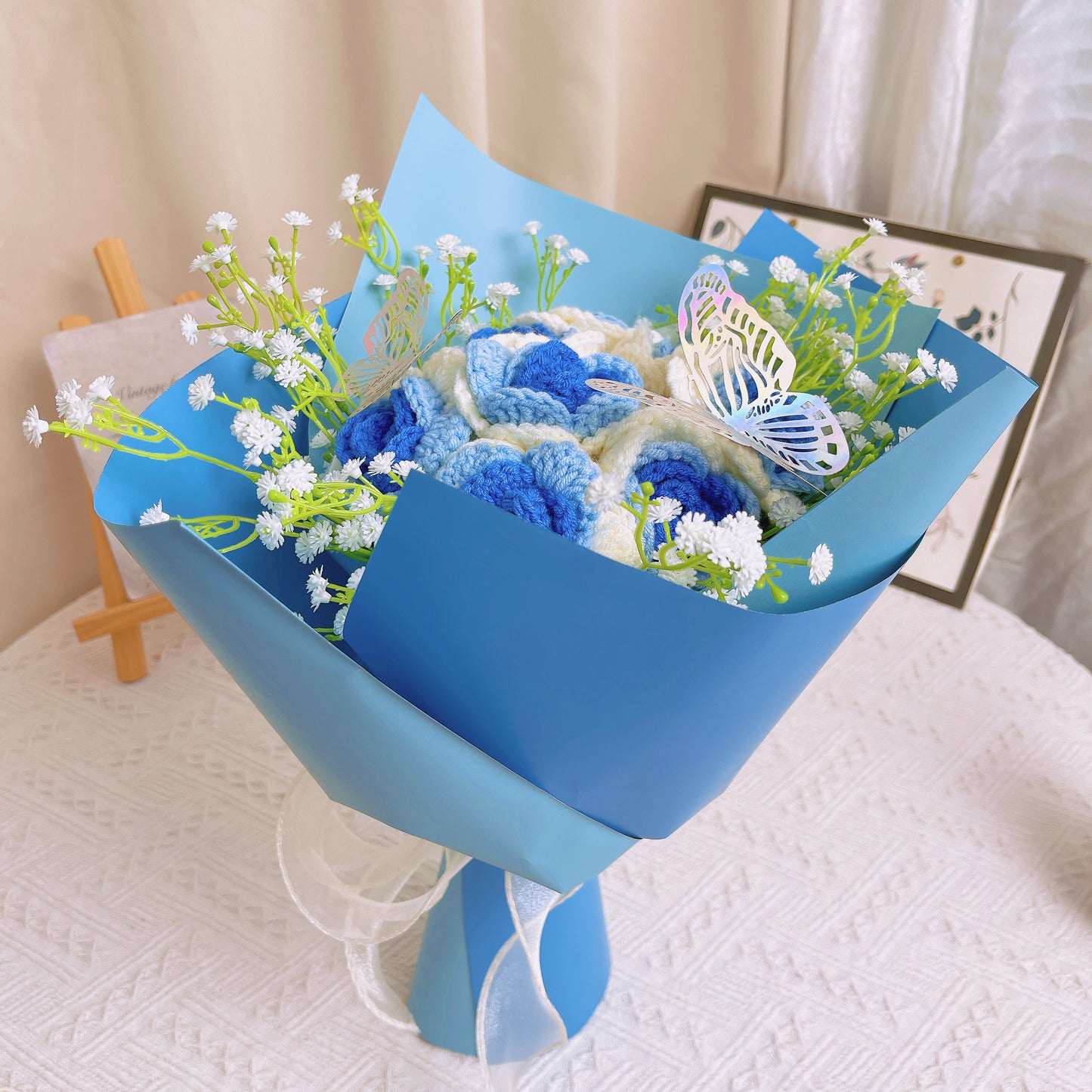 Bouquet de Roses Gradientes de Branco a Azul Congeladas com Espinhas de Bebê Branco e Acentos Vibrantes de Borboletas Coloridas, Belamente Embalado em Papéis Azul Claro e Escuro, Ideal para Celebrações como de uma Princesa