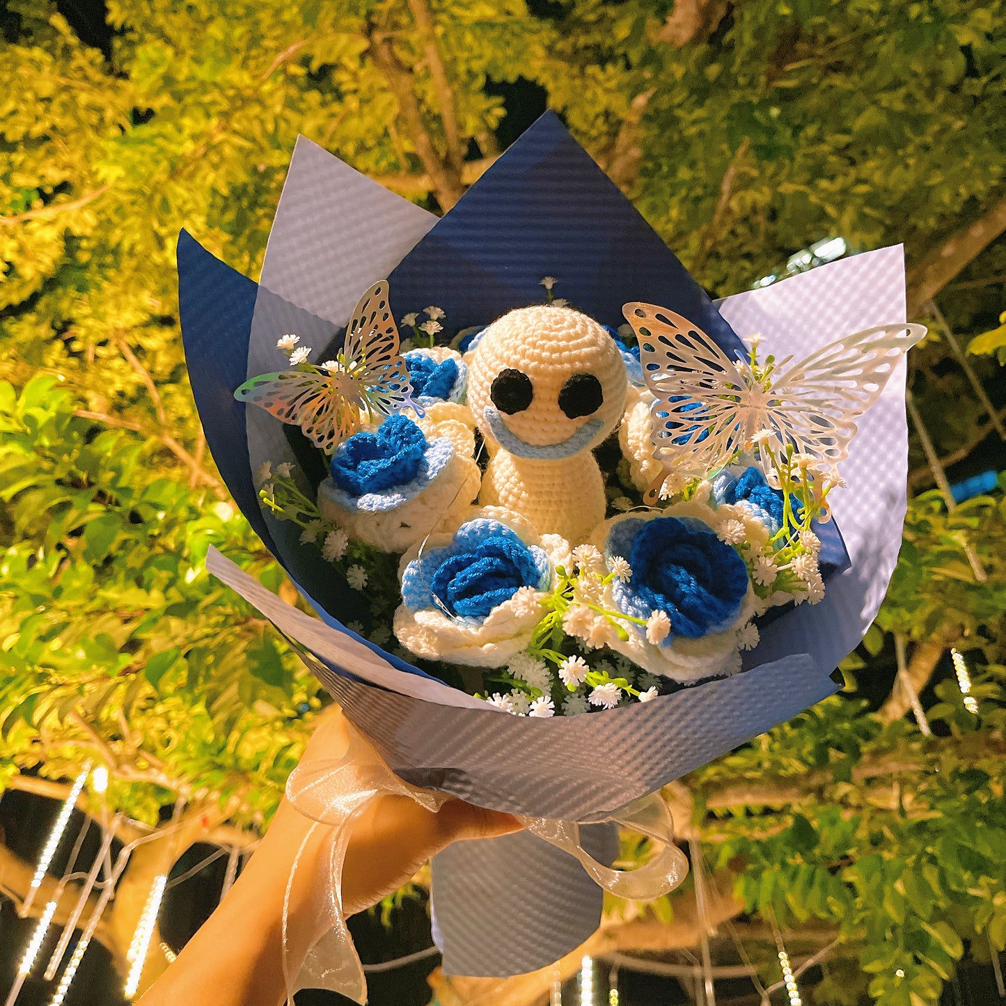 Gefrorener Rosenstrauß mit Farbverlauf von Weiß nach Blau, weißem Schleierkraut und leuchtend bunten Schmetterlingsakzenten, wunderschön verpackt in hell- und dunkelblauem Papier, ideal für Feiern im Prinzessinnenstil.