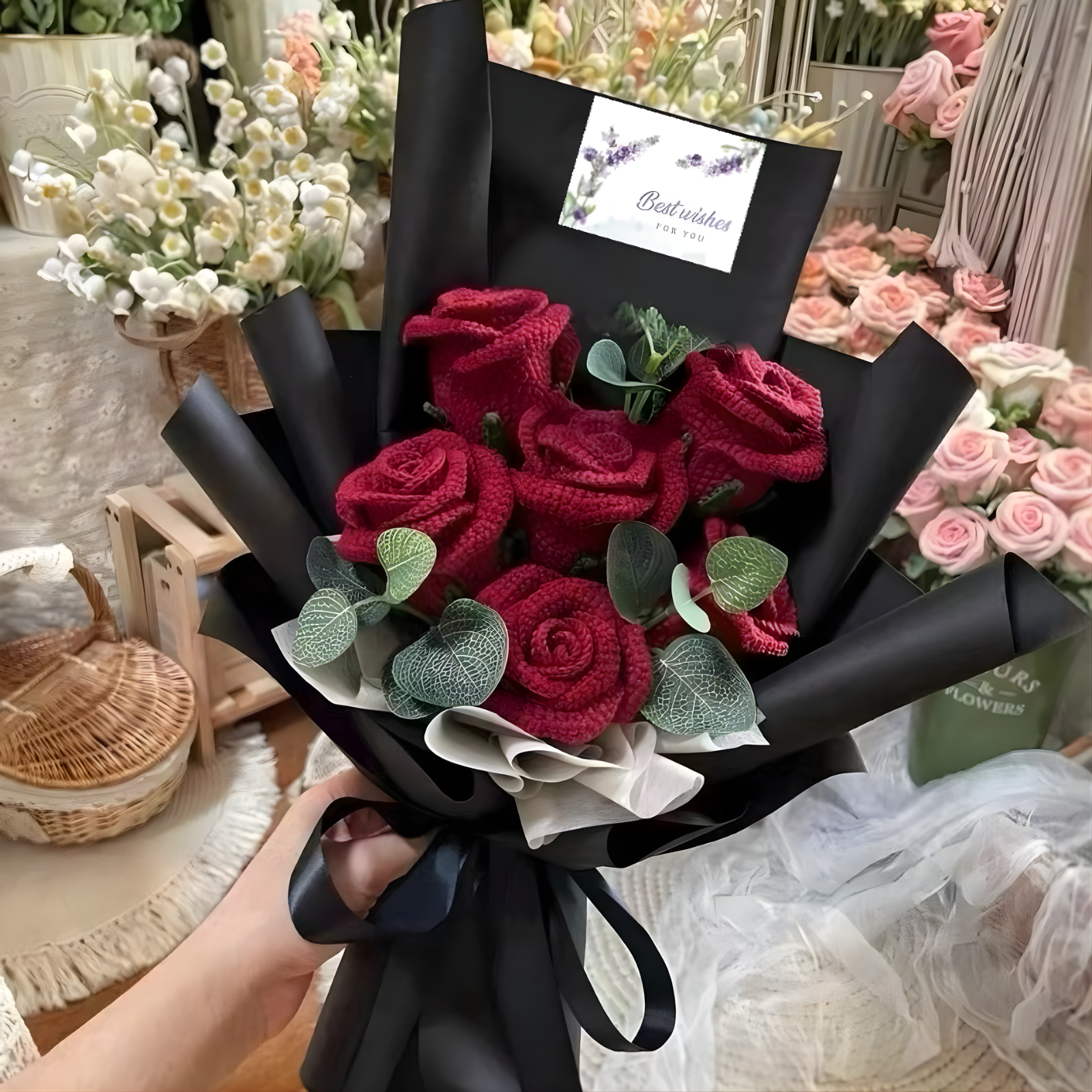 Bouquet of red roses wrapped in black paper with a visible brand tag, held by a person.