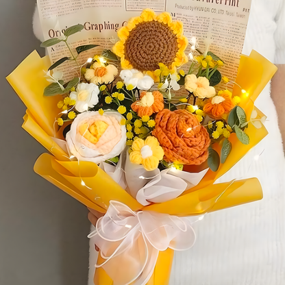 Bouquet of knitted flowers with sunflowers, roses, and other floral elements on a yellow paper.