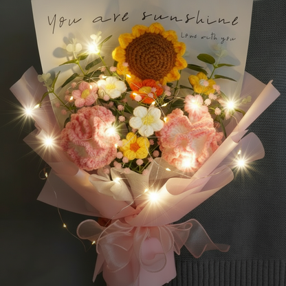A crocheted bouquet imitating sunflowers, carnations, and other flowers, wrapped in pink paper with a card that reads 'You are sunshine. Love always.