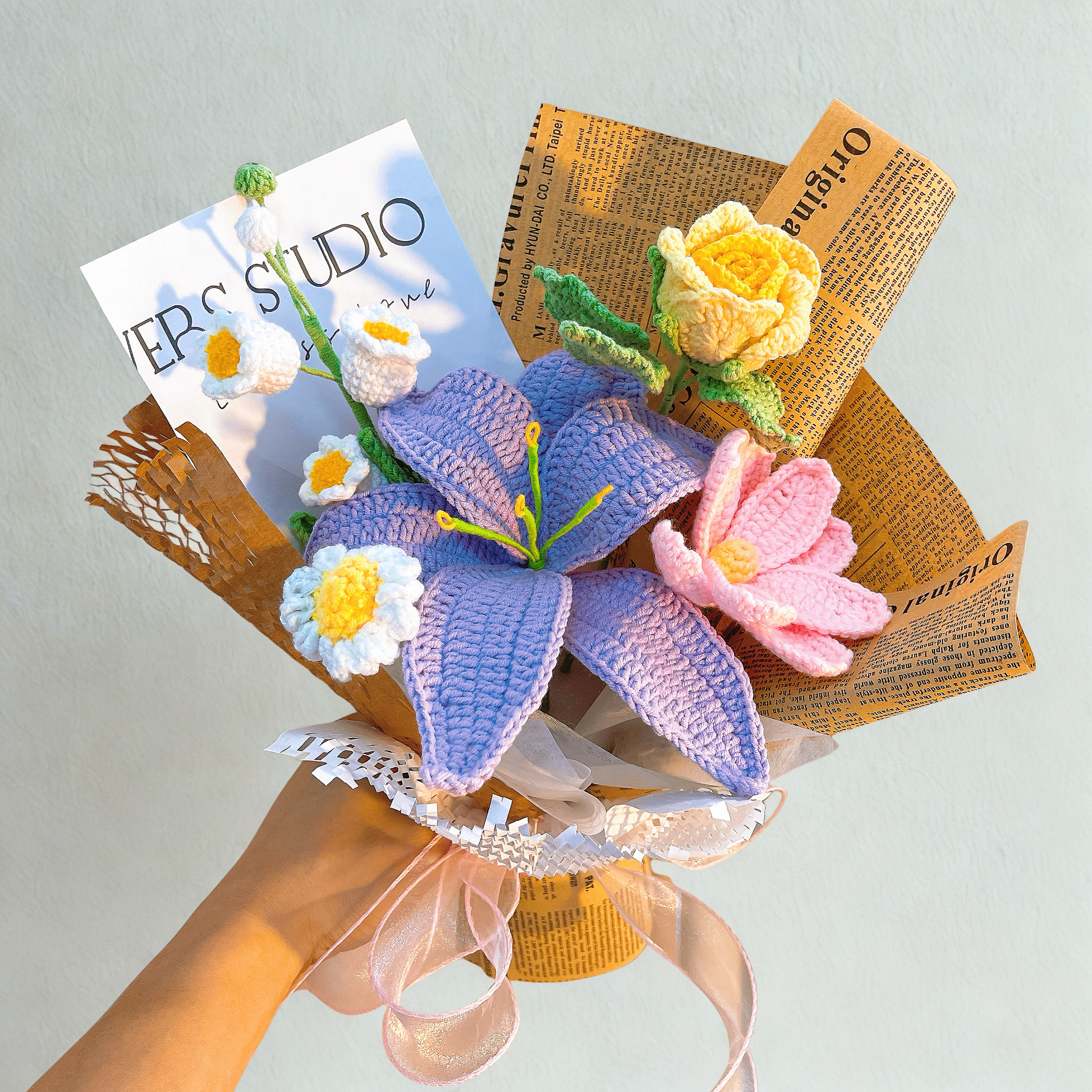 Bouquet of knitted flowers on a newspaper base with a magazine cover in the background.