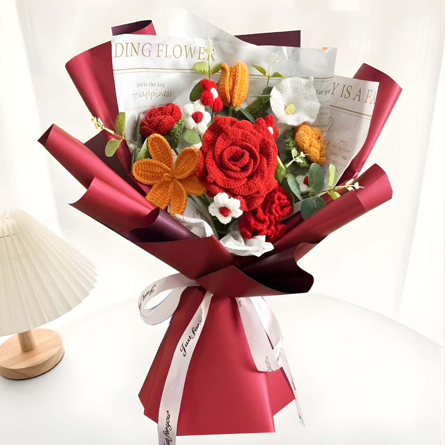 Bouquet of red and orange flowers wrapped in red paper with a white ribbon on a white background.