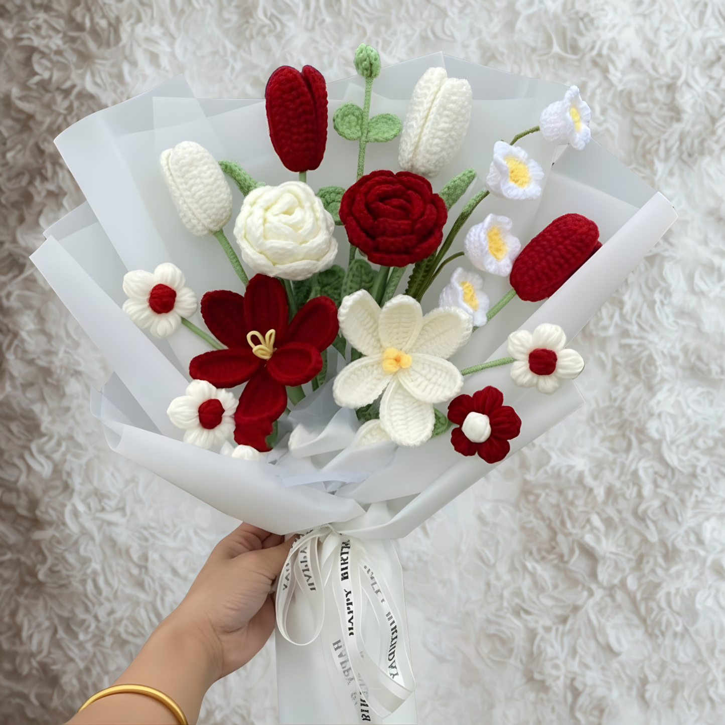 Bouquet of red and white flowers made of yarn held by a hand on a textured white background