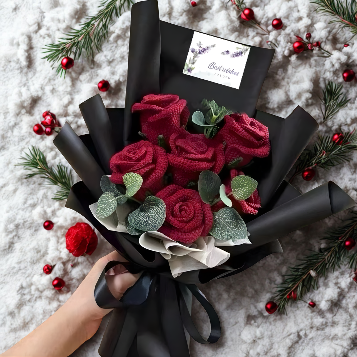Bouquet of red roses wrapped in black paper with a hand holding it, on a snowy background.