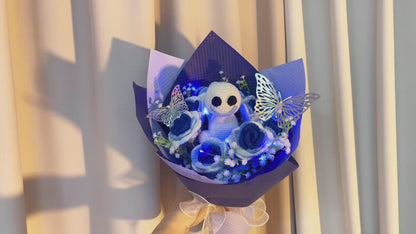 Gefrorener Rosenstrauß mit Farbverlauf von Weiß nach Blau, weißem Schleierkraut und leuchtend bunten Schmetterlingsakzenten, wunderschön verpackt in hell- und dunkelblauem Papier, ideal für Feiern im Prinzessinnenstil.