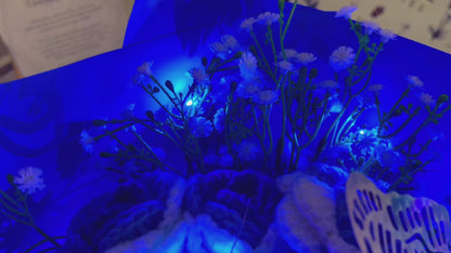 Bouquet de Roses Gradientes de Branco a Azul Congeladas com Espinhas de Bebê Branco e Acentos Vibrantes de Borboletas Coloridas, Belamente Embalado em Papéis Azul Claro e Escuro, Ideal para Celebrações como de uma Princesa